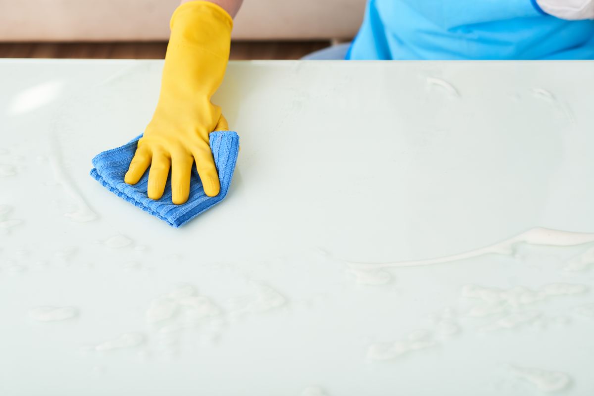 Gloved hand wiping a white table with a blue cloth during a deep cleaning