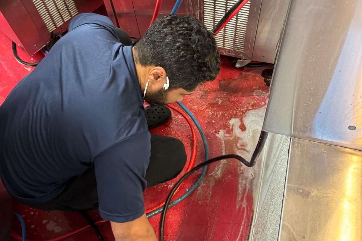 Maggie's Magic Touch team member detail-cleaning floor edges in a commercial kitchen
